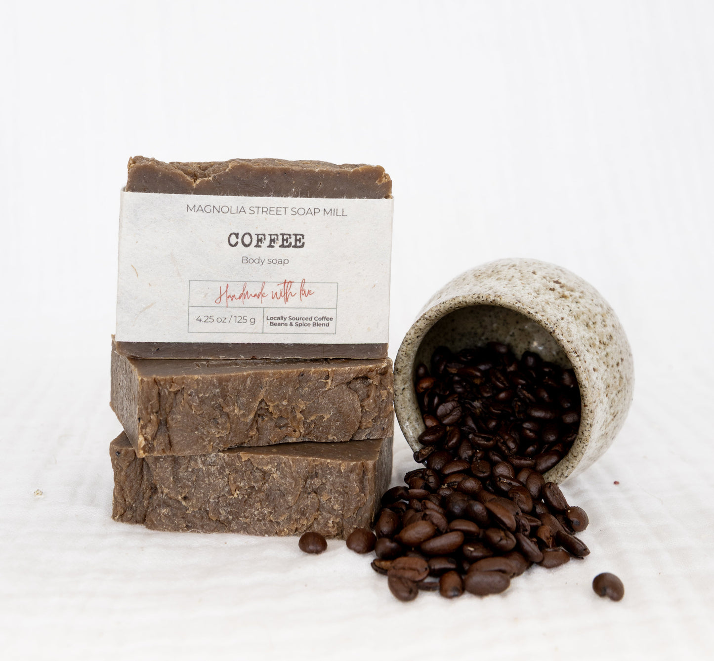 Bar of coffee soap with a container of coffee beans on a white background