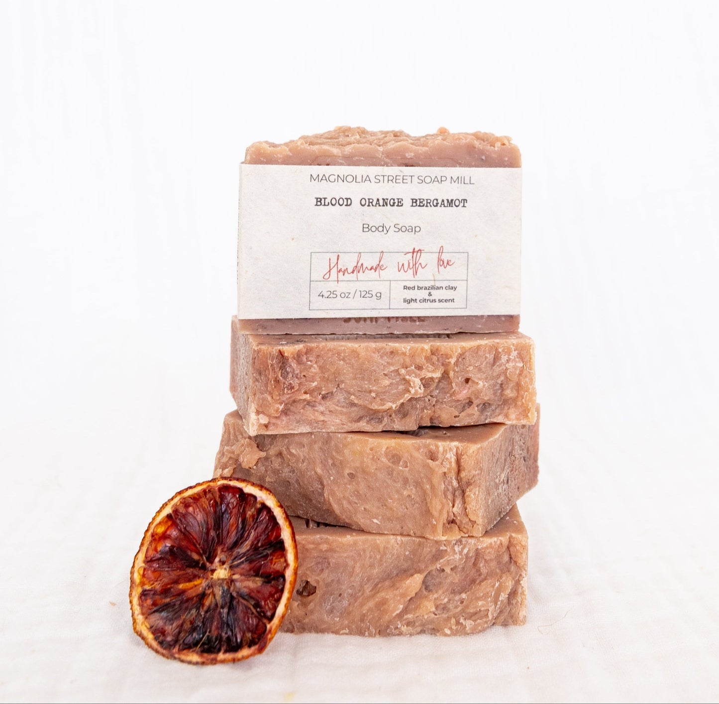 Stack of four handmade bars of soap with a dried blood orange on a white background