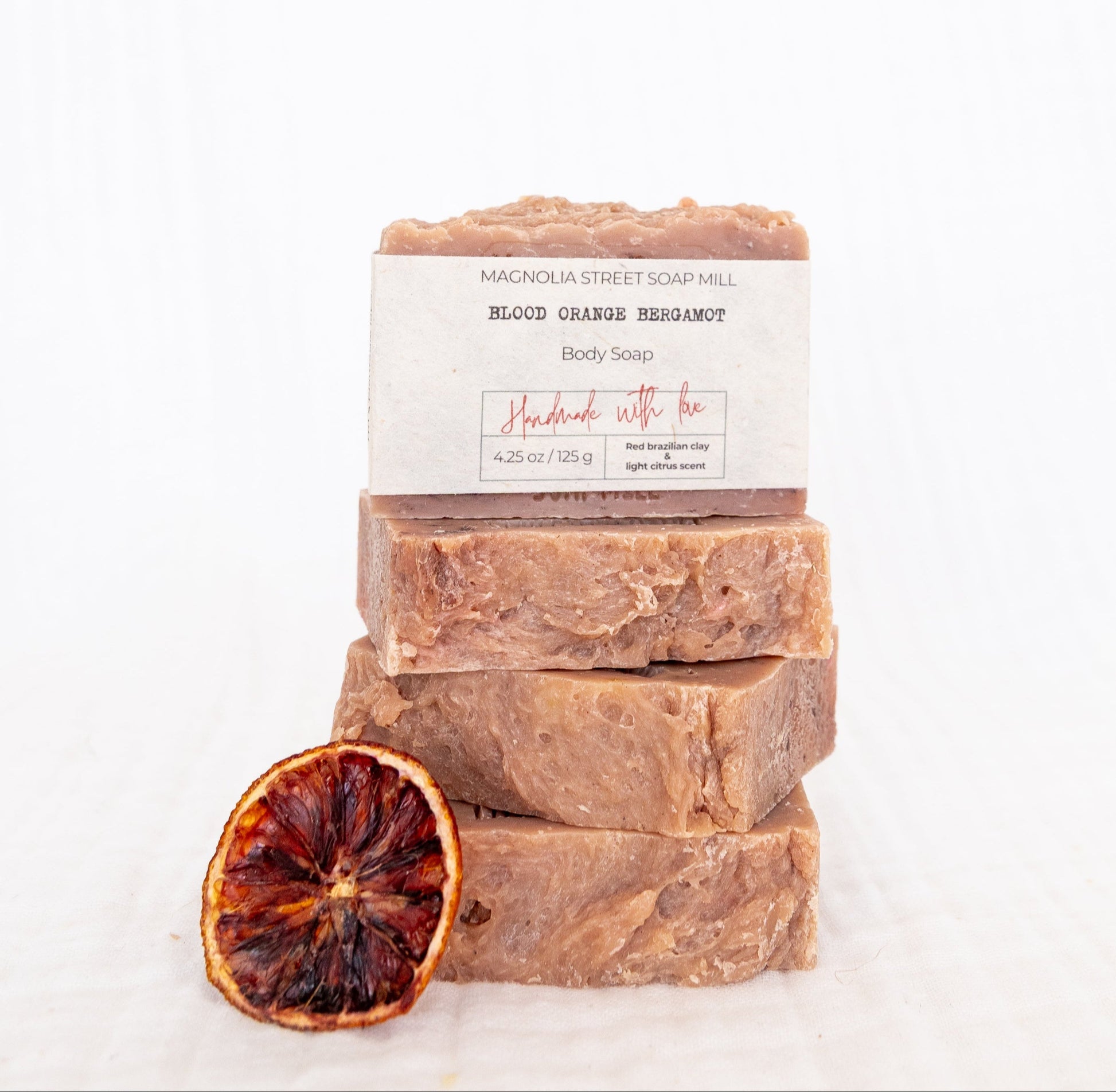 Stack of four handmade bars of soap with a dried blood orange on a white background