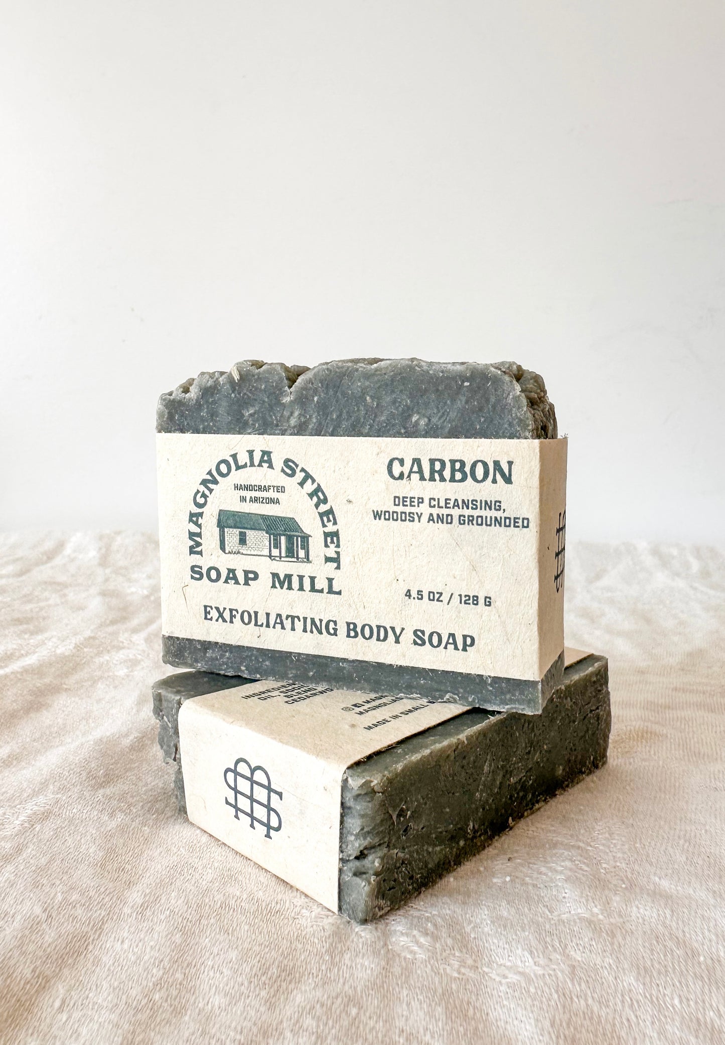 Two bars of exfoliating body soap from Magnolia Street Soap Mill on a textured surface.
