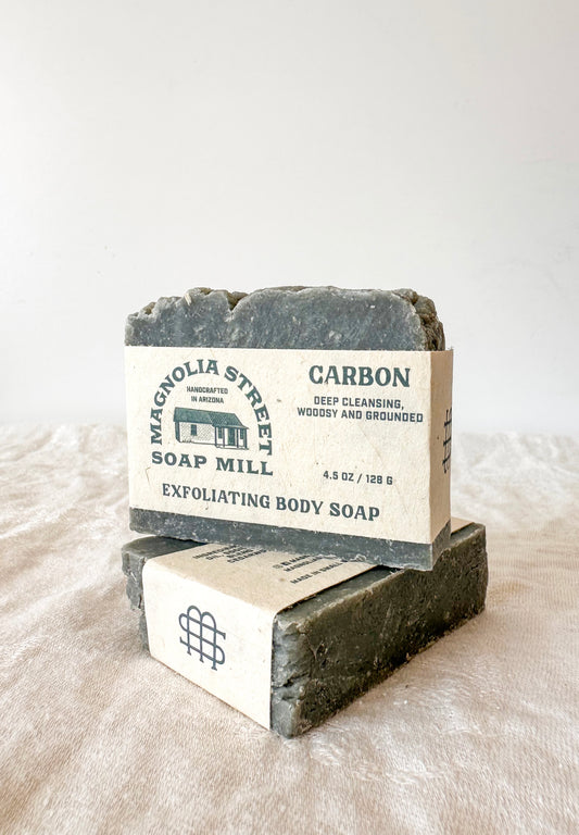 Two bars of exfoliating body soap from Magnolia Street Soap Mill on a textured surface.