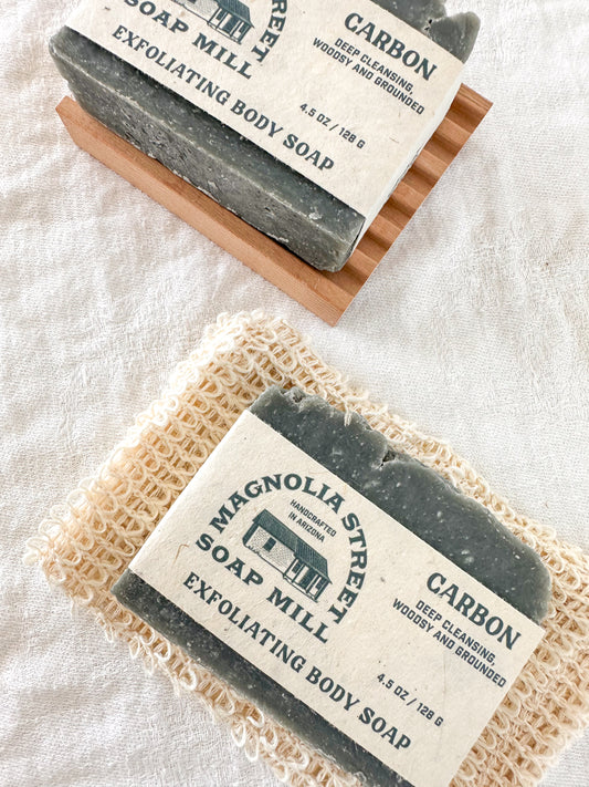 Two bars of Magnolia Street Soap Mill carbon exfoliating body soap on a textured surface.