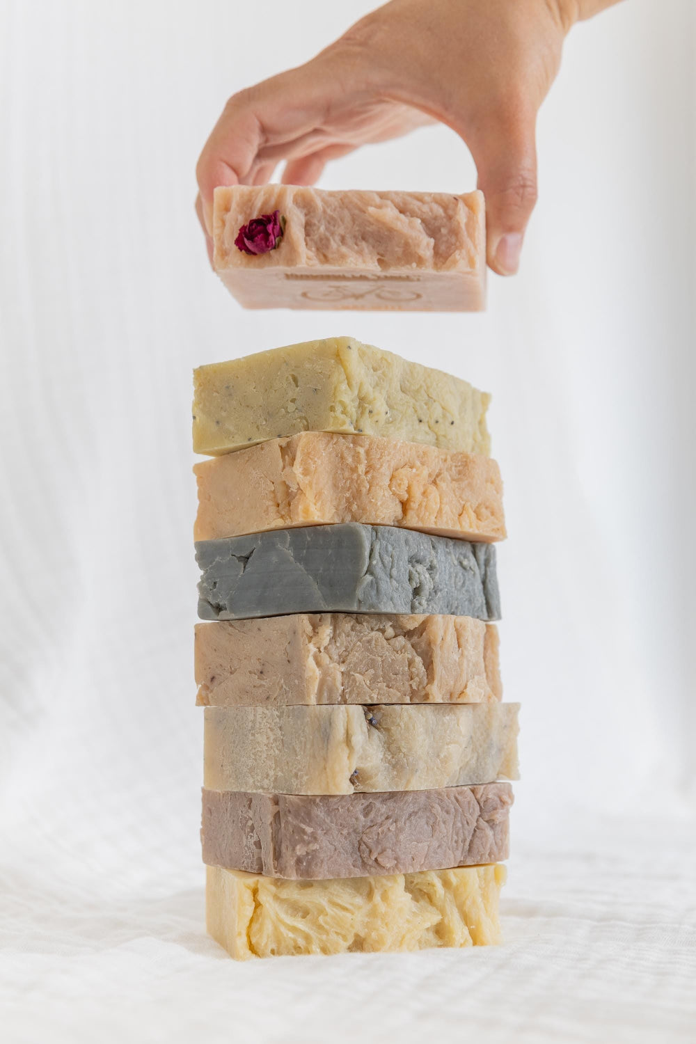 Photo of 8 handmade natural soaps stacked one on another with a hand appearing to stack the last soap.
