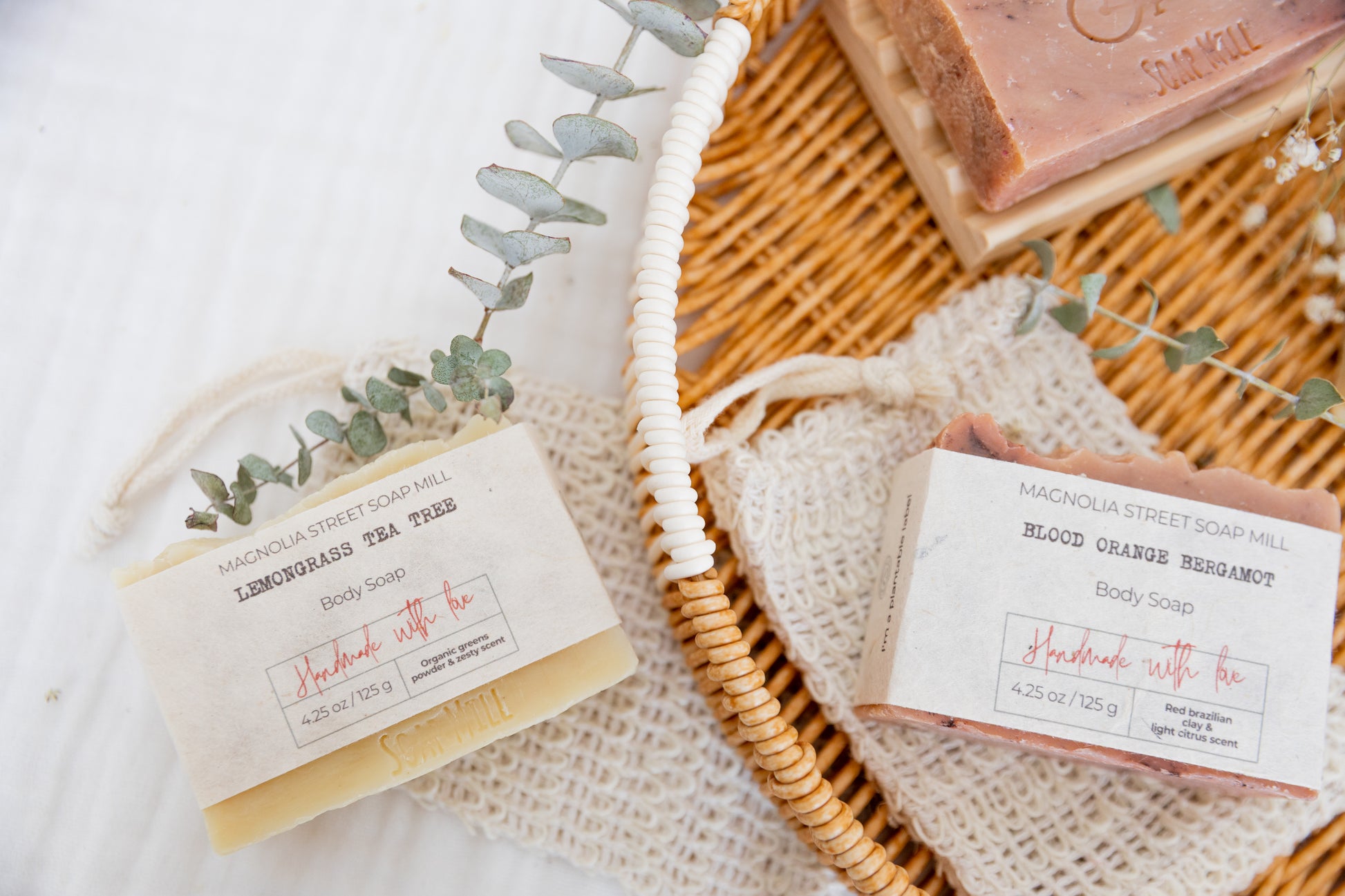 Lemongrass Tea Tree Soap next to basket with blood orange bergamot bar soaps with eucalyptus and baby breath in background.