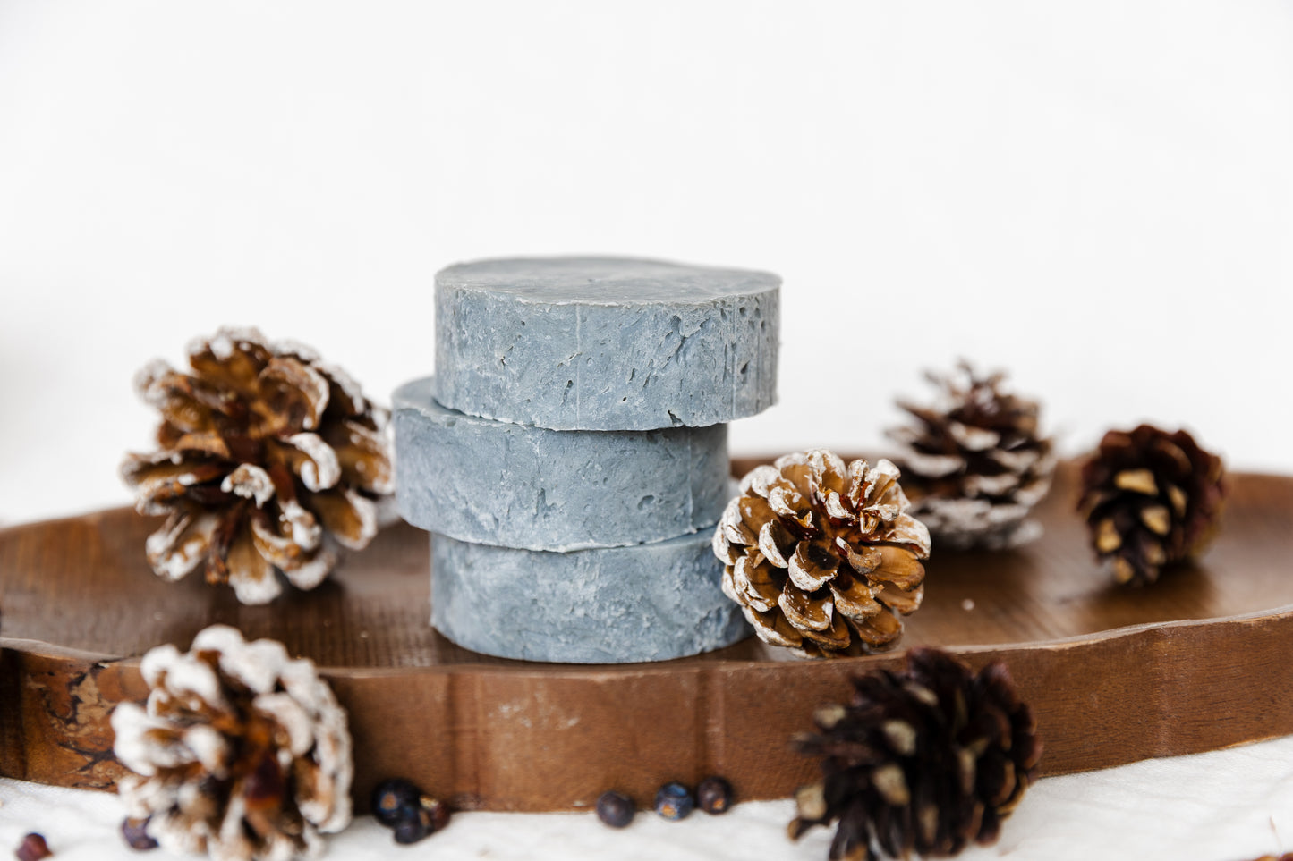 unlabeled stack of lump of coal soap pucks on wooden plate with pine cones surrounding.