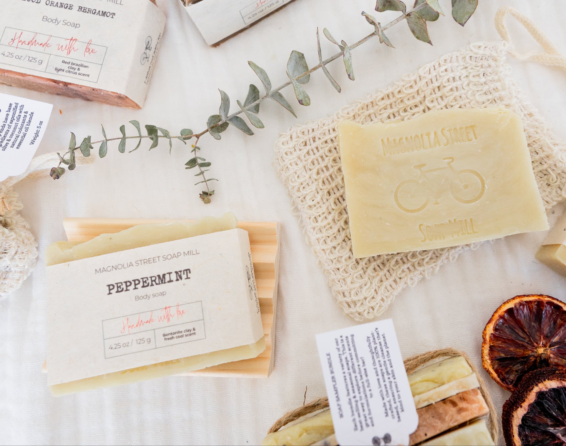 Group shot of peppermint bar soaps with other handmade soaps. Eucalyptus leaves and dried oranges in background. 
