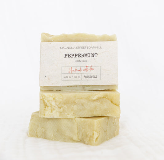 Three bars of peppermint soap stacked on white cloth with white background.