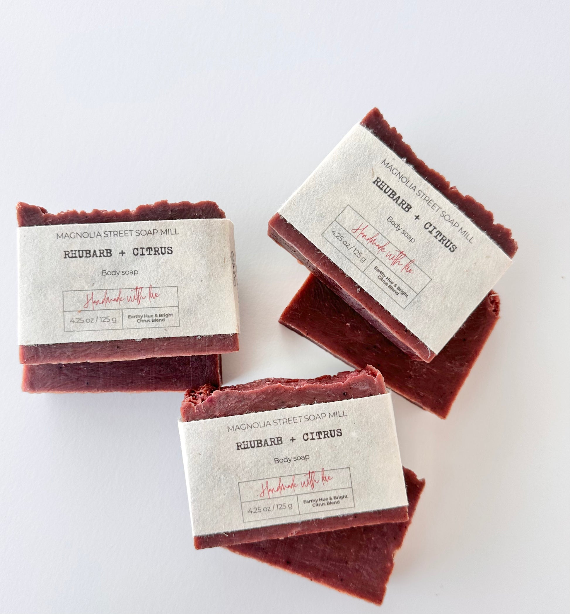 Six bars of handmade soap naturally colored with rhubarb powder wrapped in seed paper labels on a white background
