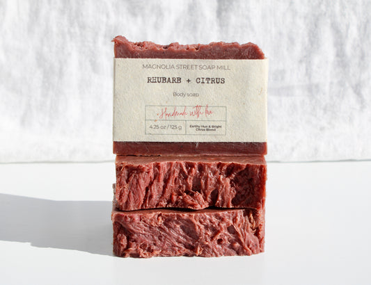 Three bars of our handmade, natural rhubarb and citrus soap wrapped in seed paper label, stacked on a white background.