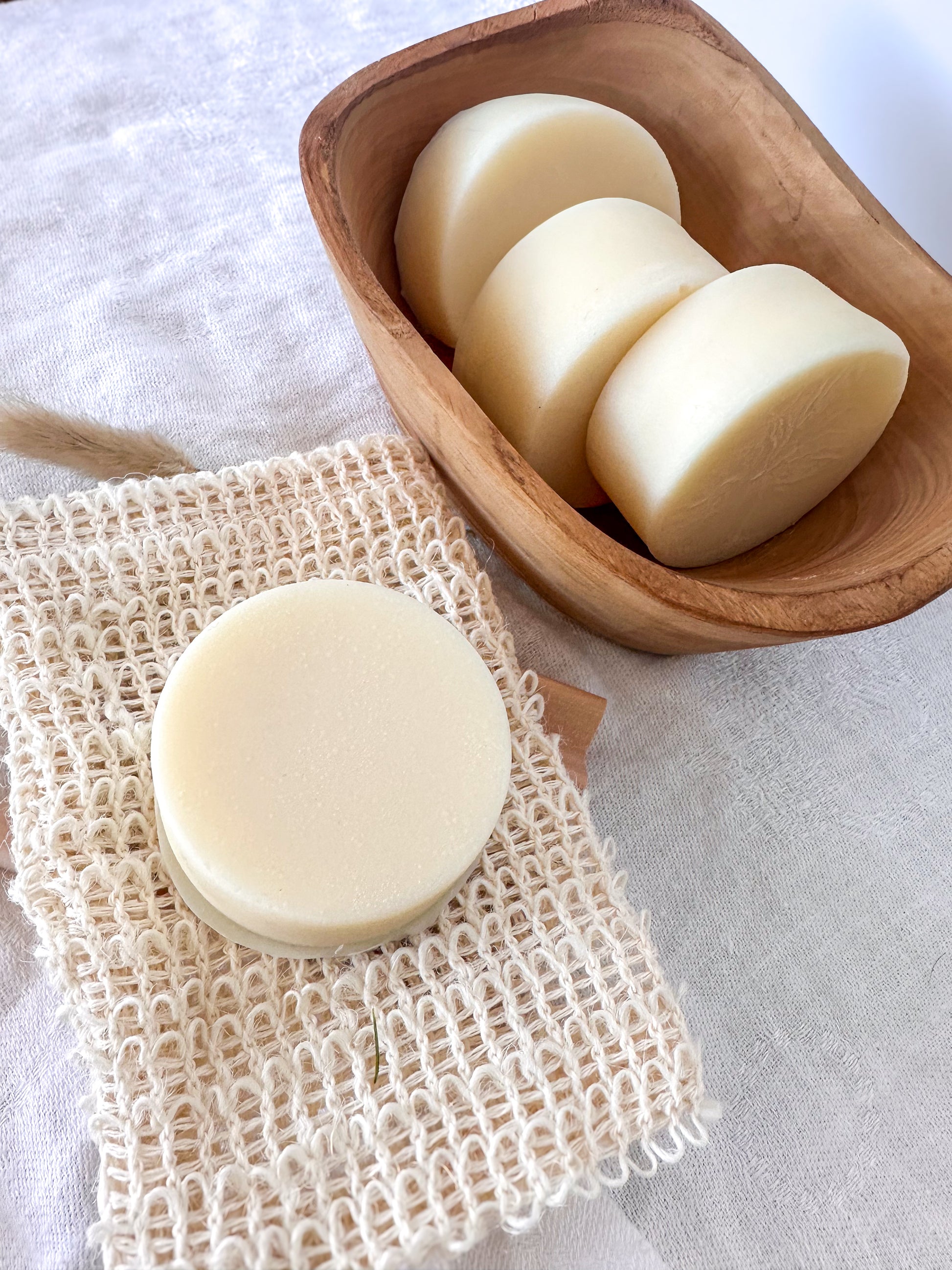conditioner bar on a natural fiber soap dish with additional bars in a wooden bowl.
