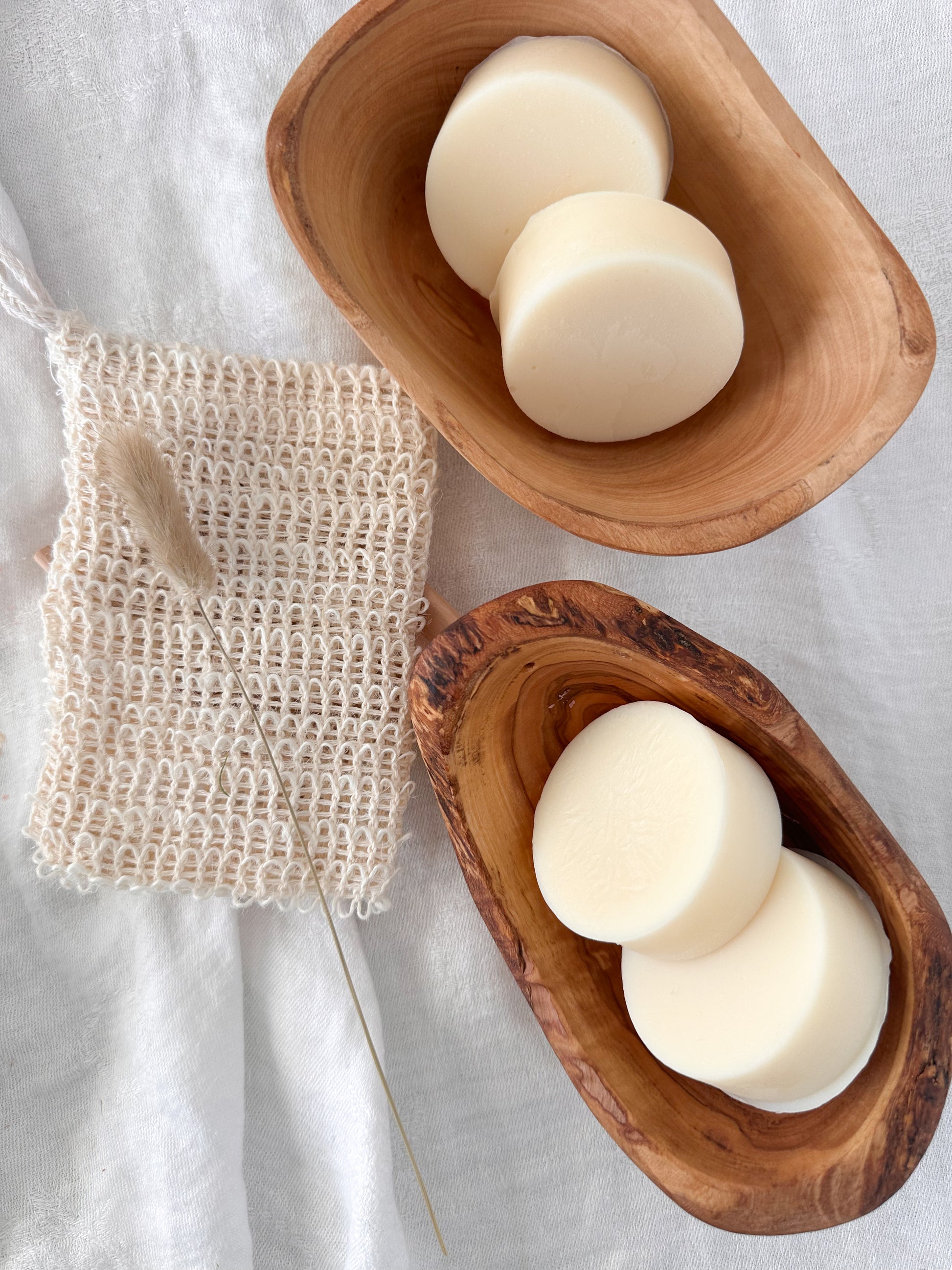 Three white conditioner bars in wooden bowls on a light fabric background